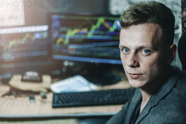 A man in an office setting with multiple monitors displaying graphs, suggesting a business atmosphere