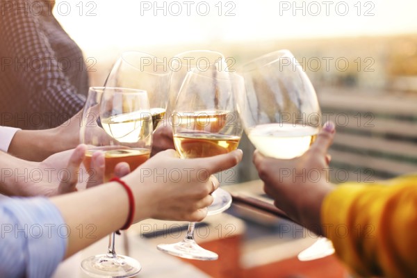 Group of anonymous people clinking wineglasses and proposing toast during party on rooftop