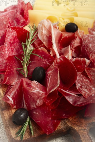 Assorted meat, appetizer, prosciutto, salami and ham, with maasdam cheese and olives, on a wooden board, breakfast, top view, close-up, no people