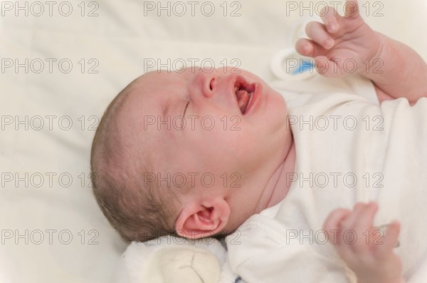 Newborn baby crying, close-up of baby lying in bed