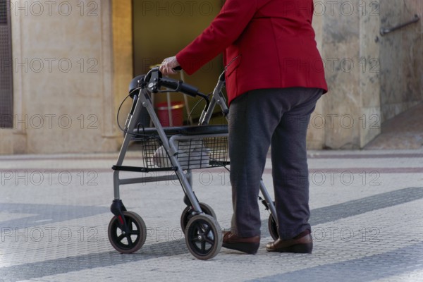 Elderly woman walking along a pedestrian street leaning on her wheeled walker