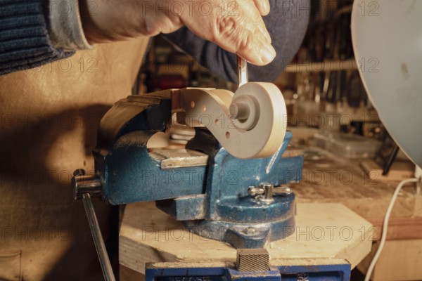 Italian luthier is meticulously shaping the scroll of a violin using a gouge, with the piece securely held in a vise within his workshop, illuminated by a warm light