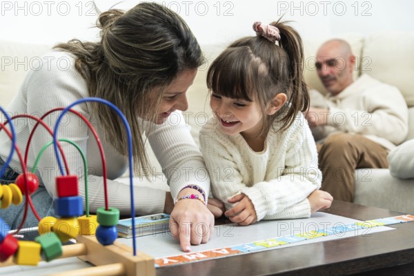 Happy family playing with alphabet puzzle, mother teaching daughter letters, father watching them, educational games for children, early childhood development
