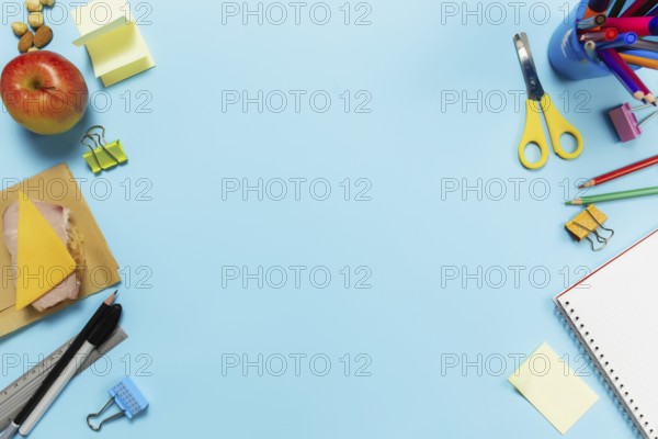 Flat lay with school, work or creativity concept with various schooling accessories, pens, pencil, notepad, paper clips, apple, nuts, sandwich, ruler, scissors, paper sticker on blue background