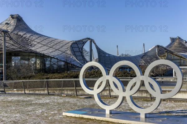 Sculptures of the Olympic rings and in the background the Olympic site with the Olympic buildings with blue sky in the background, Munich, Upper Bavaria, Bavaria, Germany, Europe