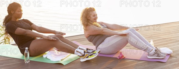 Side view female friends doing crunches by lake