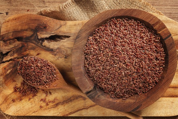 Natural, red rice, in a wooden bowl and spoon on a wooden surface in rustic style, top view