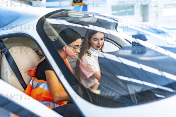 Two female pilots, one in uniform and the other in a safety vest, collaborate inside an aircraft cockpit, focusing on flight controls
