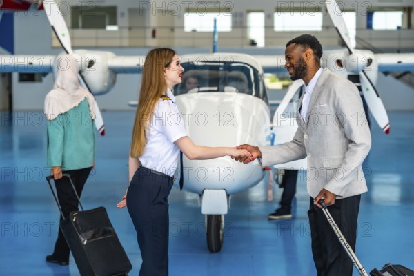 Female pilot shaking hands with businessman inside an aircraft hangar, greeting a passenger before a private flight