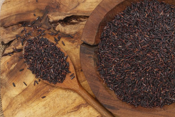 Natural black rice in a wooden bowl and spoon on a wooden surface in rustic style, top view