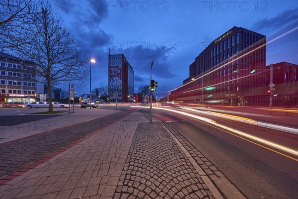 General architecture, modern building, bare wintry trees, traffic lights, pavement made of paving slabs, asphalt, car headlights, light traces, blue hour in the evening, blue evening sky, cumulus clouds, intersection between Celler Straße, Goseriede and Otto-Brenner-Straße, Hanover, state capital, Hanover region, Lower Saxony, Germany, Europe