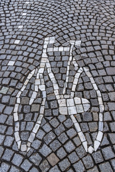 A bicycle mosaic is skilfully integrated into a street of paving stones, traffic, bicycle road, street
