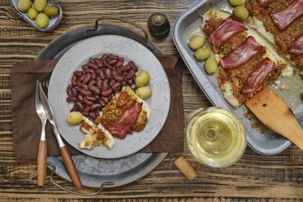 A delectable plate of fish topped with herbs and meat is presented alongside kidney beans and green olives