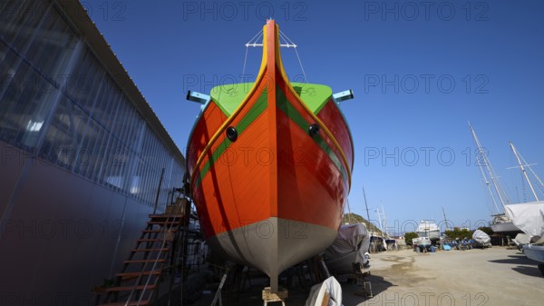 Large orange boat in a shipyard in front of a blue sky, boatyard Diakofti, new construction of a coloured wooden boat, Diakofti, Patmos, Dodecanese, Greek Islands, Greece, Europe