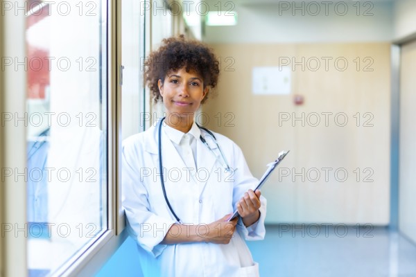 Female doctor standing confidently in a bright hospital corridor, holding a medical chart and smiling with professionalism and warmth