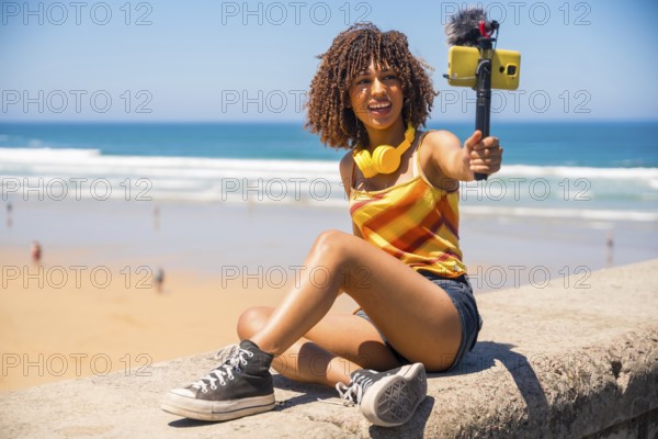 Influencer filming a vibrant vlog on a stunning beach, capturing moments with a smartphone and an external microphone while enjoying summer vibes