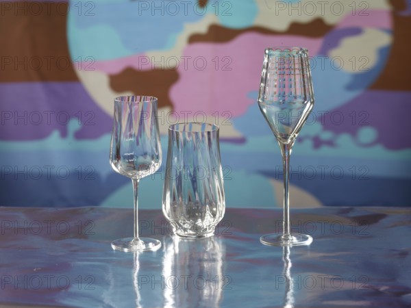 Various glasses on silver foil, behind them various colour elements, studio shot