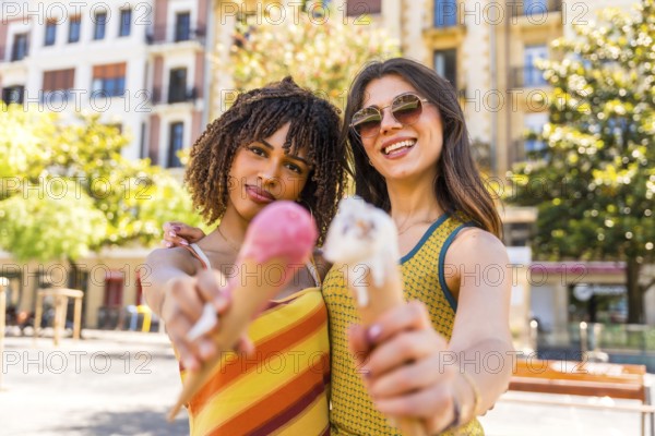 Two friends enjoying a sunny day in the city, happily holding and sharing colorful ice cream cones while smiling in the warm sunshine
