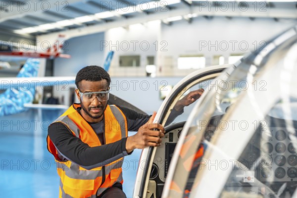 Aircraft maintenance engineer wearing safety glasses and a high visibility vest, performing a pre flight inspection on a small airplane inside an aircraft hangar