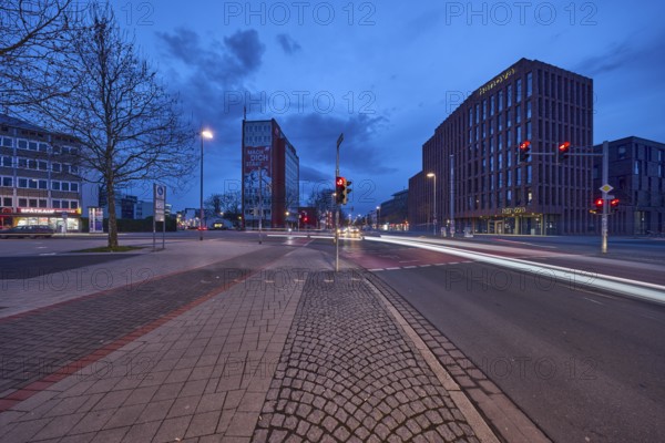General architecture, modern building, bare wintry trees, traffic lights, pavement made of paving slabs, asphalt, car headlights, light traces, blue hour in the evening, blue evening sky, cumulus clouds, intersection between Celler Straße, Goseriede and Otto-Brenner-Straße, Hanover, state capital, Hanover region, Lower Saxony, Germany, Europe