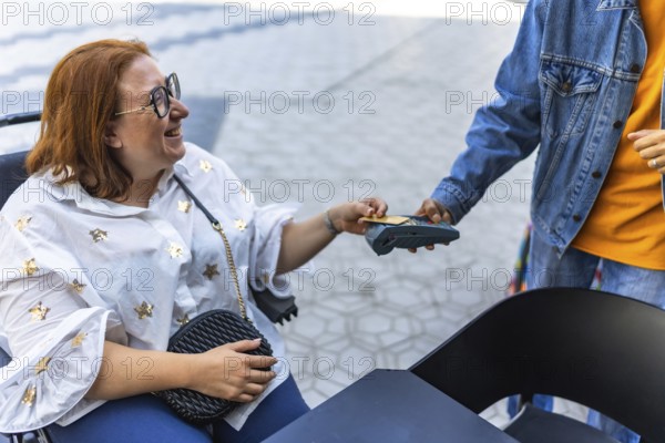 Happy customer using a credit card for contactless payment at an outdoor cafe, assisted by a friendly waitress