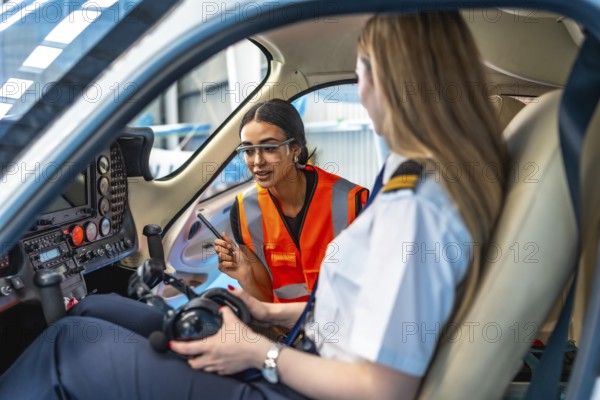 Aircraft maintenance engineer is explaining something to a pilot sitting in the cockpit of a small plane