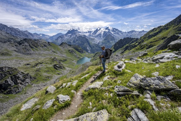Mountaineer on hiking trail in mountain landscape, descent at Col du Louvie, view of mountain lake Lac du Louvie and glaciated mountain peaks of the Grand Combine, Valais Alps, Val de Bagnes, Valais, Switzerland, Europe