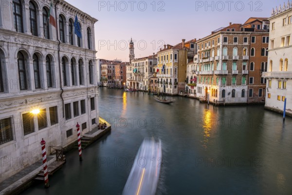 View of the Grand Canal with gondoliers at sunset, picturesque evening mood with illuminated palazzos on the canal and church tower of the Chiesa Parrocchiale dei Santi Apostoli, long exposure, view from the Rialto Bridge, Venice, Veneto, Italy, Europe