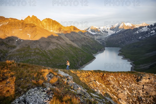 Mountaineer on the summit of Mont de la Blana, alpenglow at sunset, view of a blue mountain lake, Lac des Dix reservoir, behind mountain peak Mont Blanc de Cheilon with glacier, Hérménence, Valais Alps, Valais, Switzerland, Europe