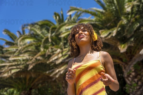 Tourist enjoying music while wearing headphones in a vibrant tropical paradise, surrounded by swaying palm trees under a sunny blue sky