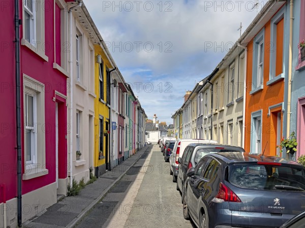 Bunte Reihenhäuser auf einer ruhigen Straße, geparkt mit Autos und blauem Himmel, Penzance, Cornwall, Großbritannien