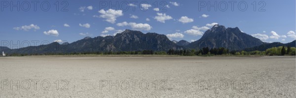Cracked, dried out ground, waterless Forggensee in spring, behind it Tegelberg massif and Säuling, Ammergau Alps, near Füssen, Ostallgäu, Bavaria, Germany, Europe