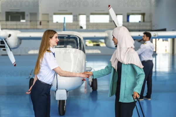Female pilot shaking hands with a muslim businesswoman inside an aircraft hangar, symbolizing partnership and collaboration in aviation