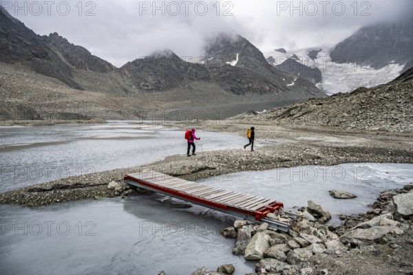 Mountaineers at a makeshift bridge over a stream, glacier river at the Glacier de Cheilon, in the background mountain peak Mont Blanc de Cheilon in clouds, Valais, Western Alps Switzerland