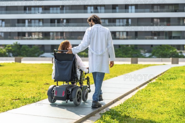 Doctor assisting a female patient in a wheelchair, strolling through a modern hospital's green outdoor area