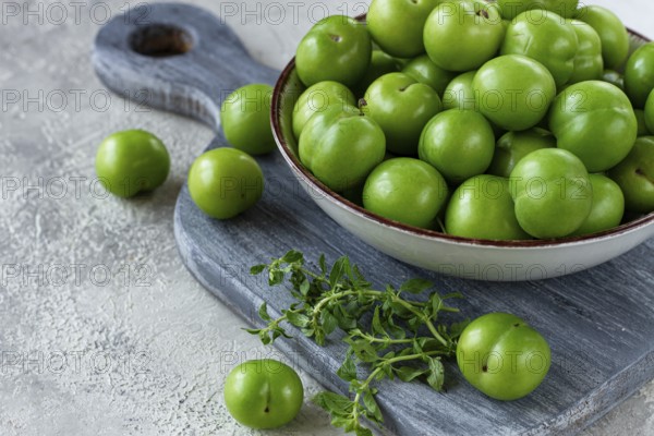Tkemali, green cherry plum, in a bowl, on a gray table, top view, natural light, no people