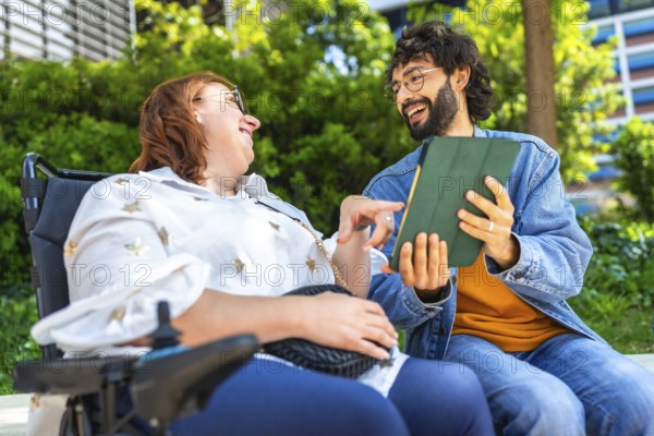 Happy woman with disability using tablet with her friend, modern lifestyle and inclusion concept, smiling people enjoying time together