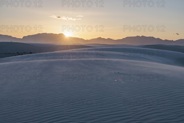 Rays of light over the mountains highlight windblown sand at sunset at White Sands National Park in Alamogordo, New Mexico, USA, North America