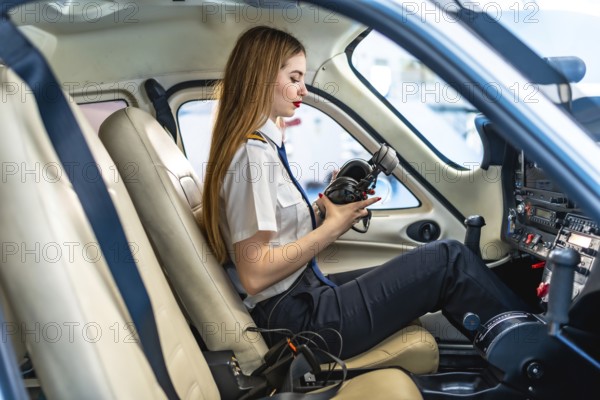 Young woman pilot checking her headset while sitting in the cockpit of a small aircraft, preparing for flight