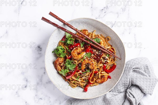 Udon noodles, shrimp with vegetables and fresh herbs, in a bowl with chopsticks, light background, homemade, no people