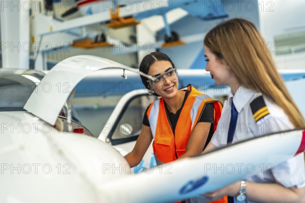 Female pilot and aircraft maintenance technician working together in hangar, discussing maintenance procedures and preparing the aircraft for flight