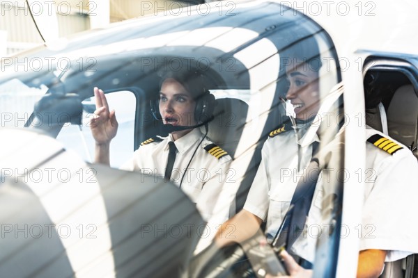 Two female pilots are communicating inside the cockpit of a private plane, preparing for takeoff