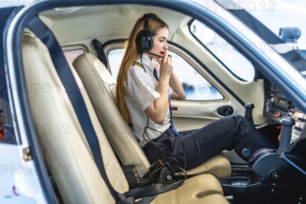 Female pilot sitting in the cockpit of a small aircraft, wearing a headset and communicating, preparing for take off