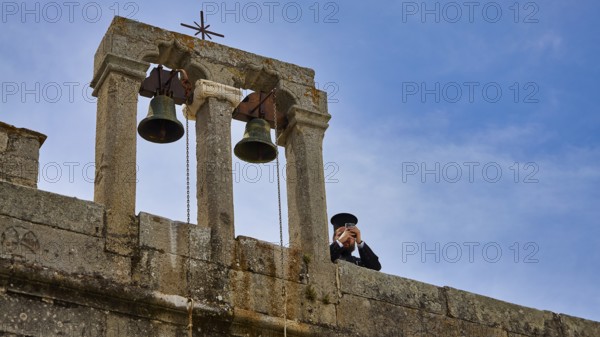 Priest next to bells on a wall in front of a blue sky, Monastery of St John the Theologian, Monastery of St John the Theologian, World Heritage Site 1999, Patmos, Dodecanese, Greek Islands, Greece, Europe