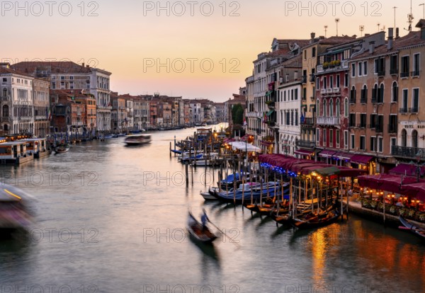 View of the Grand Canal with gondoliers at sunset, picturesque evening mood with illuminated palazzos on the canal, long exposure, view from the Rialto Bridge, Venice, Veneto, Italy, Europe