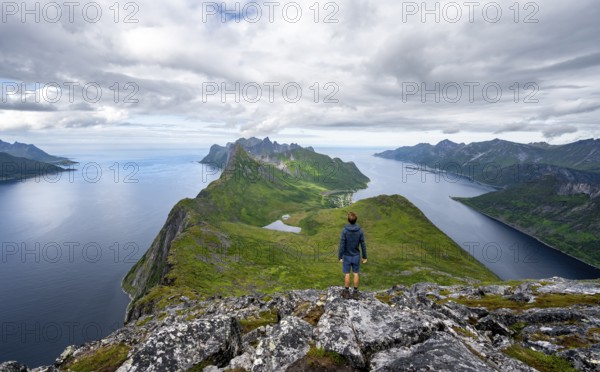View of fjords Øyfjorden and Mefjorden, mountains on the headland of Fjordgård, view from the mountain Barden, young man looking into the distance, Senja, Norway, Europe