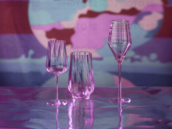 Various glasses on silver foil, behind them various colour elements, studio shot