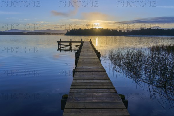 Wooden jetty reaches into the lake as the sunrise illuminates the dawn on Lake Mahinapua, Ruatapu, South Island, New Zealand, Oceania