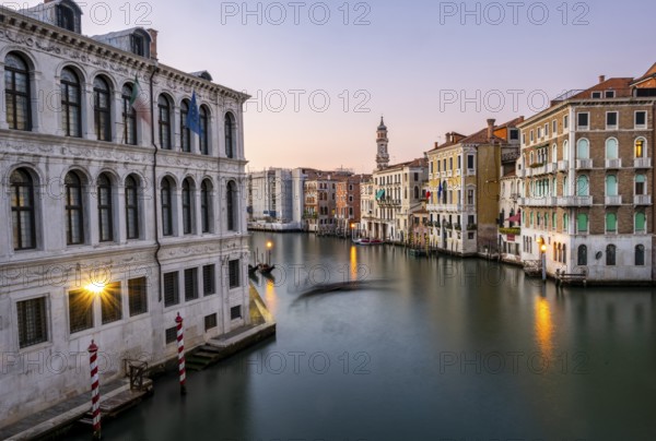 View of the Grand Canal with gondoliers at sunset, picturesque evening mood with illuminated palazzos on the canal and church tower of the Chiesa Parrocchiale dei Santi Apostoli, long exposure, view from the Rialto Bridge, Venice, Veneto, Italy, Europe