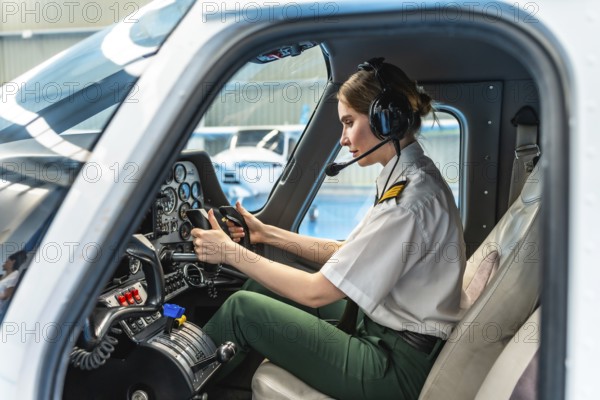 Confident female pilot wearing headset and holding steering wheel while sitting in cockpit of airplane